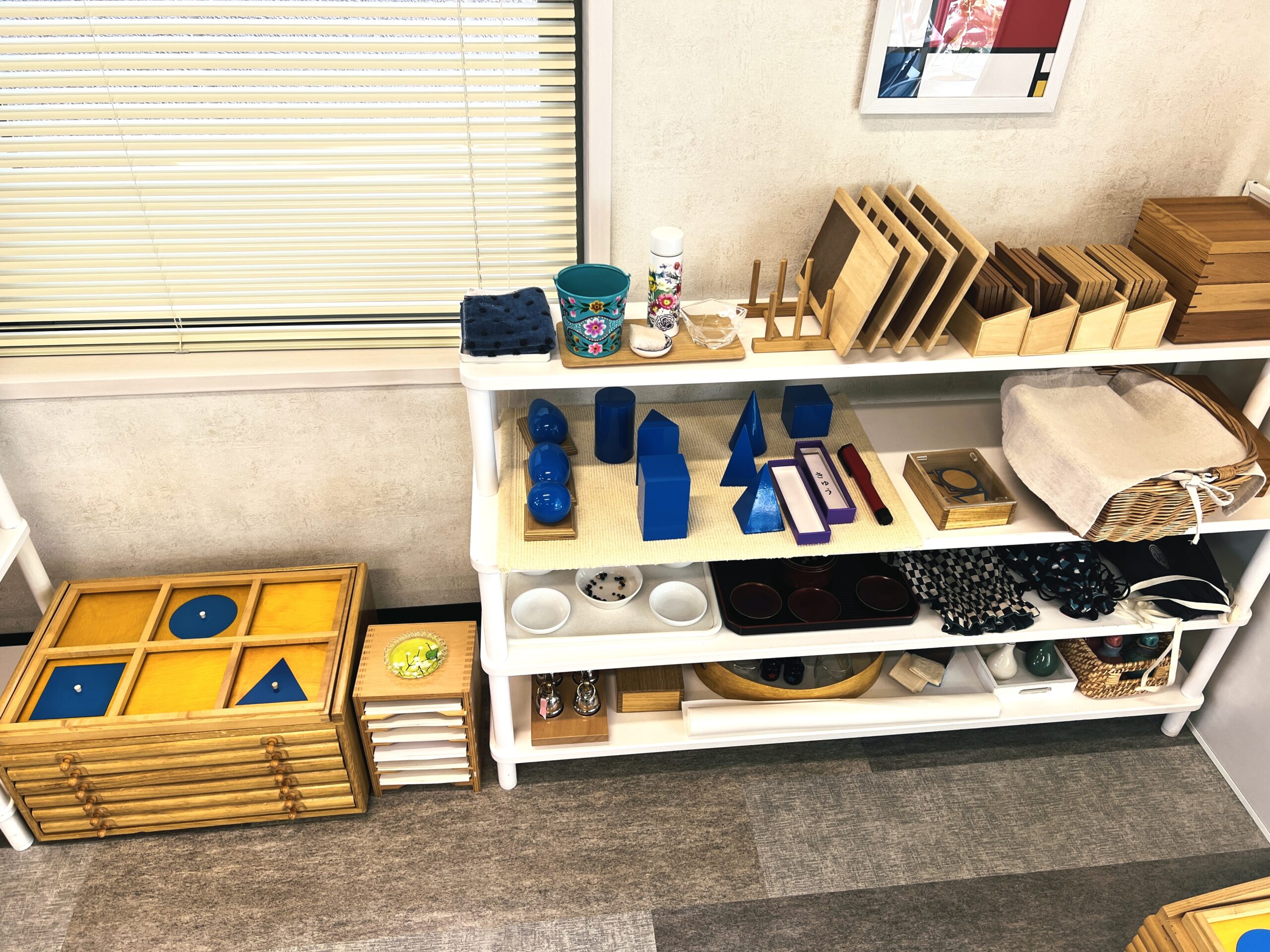 青い幾何立体や幾何図形の教具が並ぶ感覚教育の棚